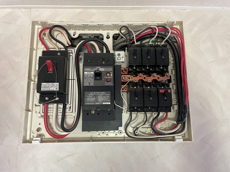 当日の現地確認：既設分電盤の内部。主幹と既存回路が入っており、エアコン用の空きスペースがない